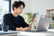 スマートフォンとノートパソコンを使い、表示や操作を確認する架空のWeb制作者。記事のために生成した写真です。